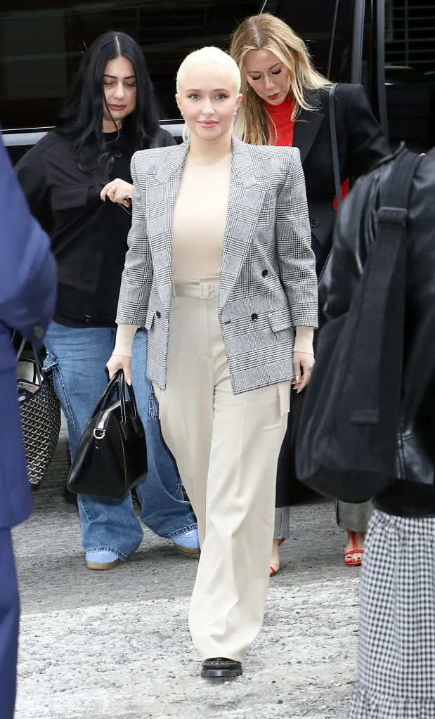 Hayden Panettiere wearing a plaid blazer, beige top, and matching wide-leg trousers, carrying a black handbag, walking alongside two other women.