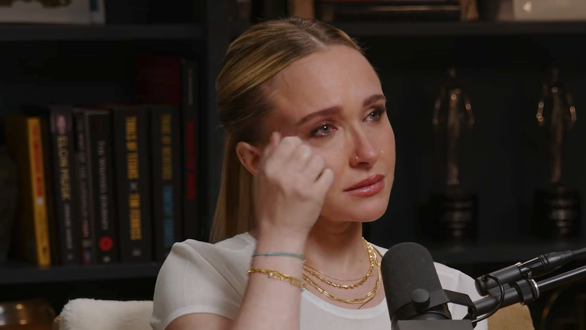 Hayden Panettiere in a white shirt crying and wiping her eye during an interview.