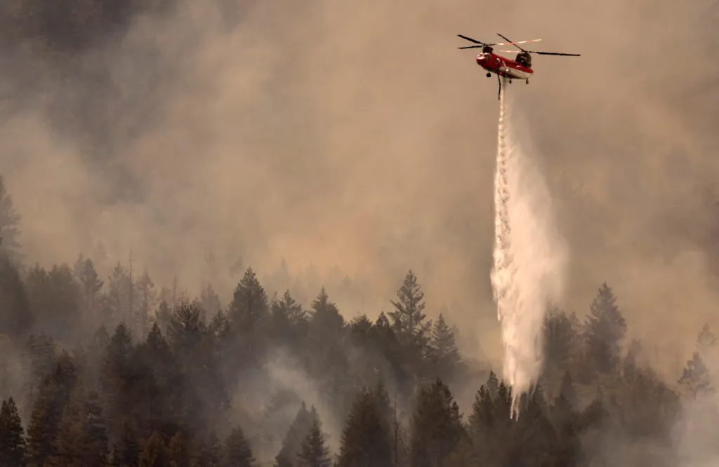A helicopter drops water on the Pickett Fire over a smoke-filled forest in Pope Valley, California.