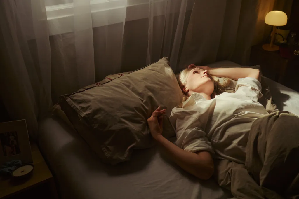 High-angle shot of a young woman lying awake in bed, staring at the ceiling, suggesting insomnia.