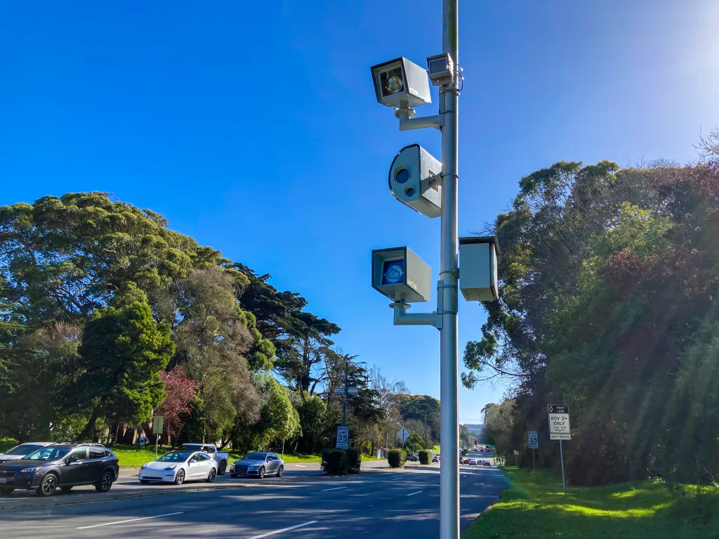 A speed camera and traffic camera stand next to a carpool (HOV) high occupancy vehicle lane in San Francisco, California.