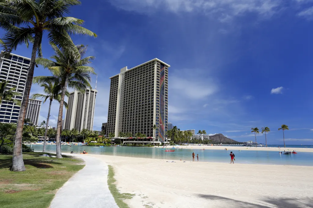 The Hilton Hawaiian Village on Waikiki Beach in Honolulu, Hawaii, with palm trees, people, and buildings.