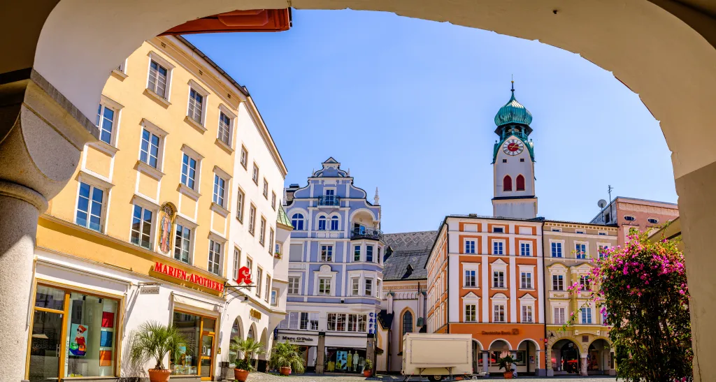 View through an archway of historic buildings in Rosenheim, Germany, with a prominent clock tower.