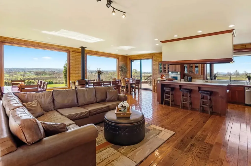 An open-plan living room and kitchen area with panoramic views of a vineyard.