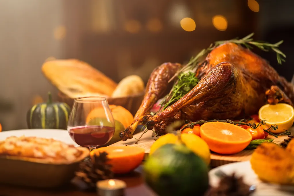 Roasted turkey and sides, including wine, bread, and fruits, on a wooden table.
