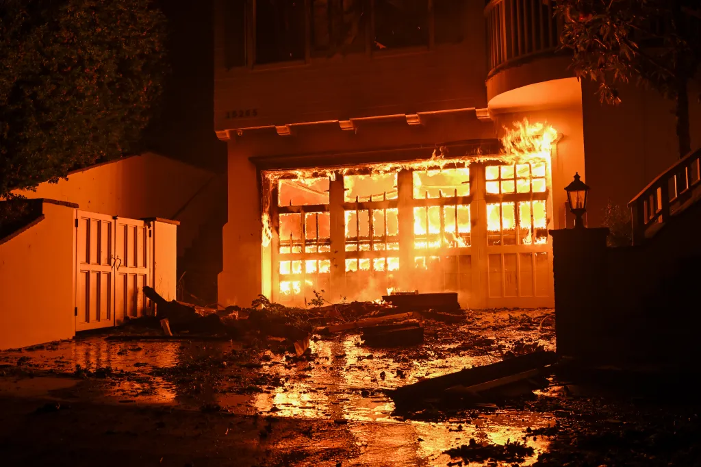 A house engulfed in flames at night during a wildfire.