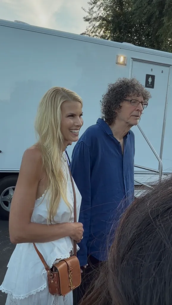 Howard Stern and Beth Ostrosky standing outside near a portable restroom.