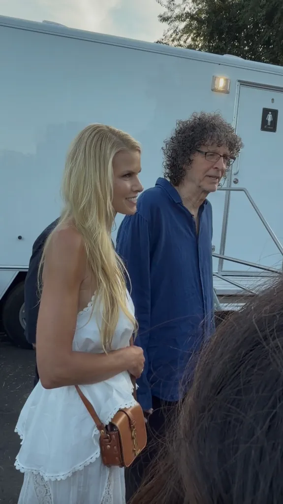 Howard Stern, with curly hair and glasses, walking with a blonde woman.