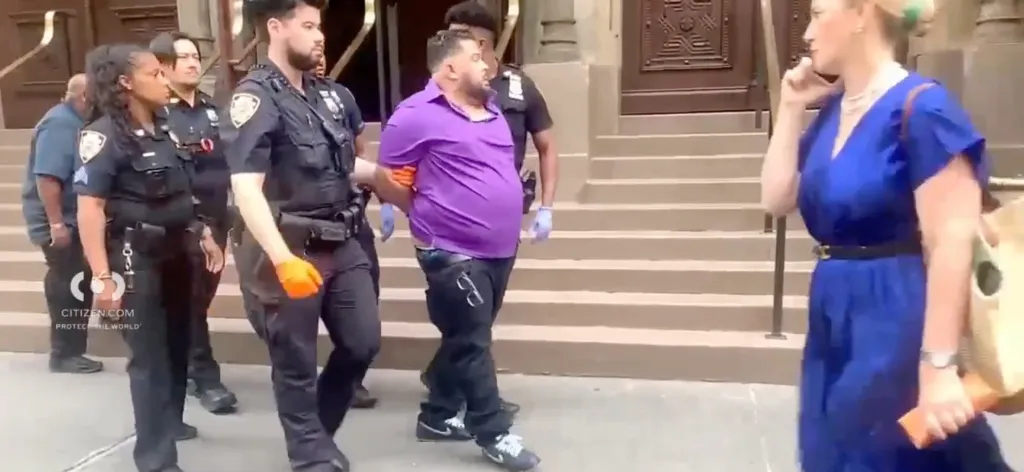 A man in a purple shirt is handcuffed by police officers.