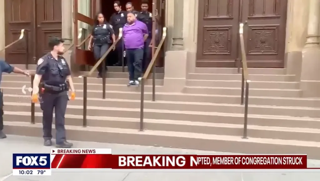 A man in a purple shirt being escorted down the steps of a building by police officers.