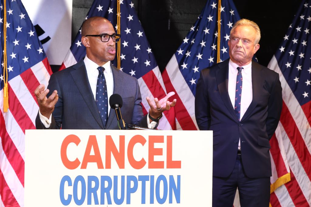 HUD Secretary Scott Turner speaking at a podium next to HHS Secretary Robert F. Kennedy, Jr. with 