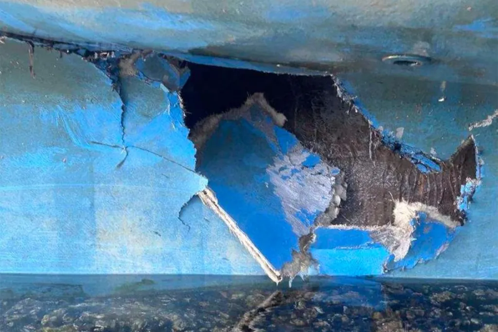 Damage to a boat hull with a large hole and peeling blue paint.