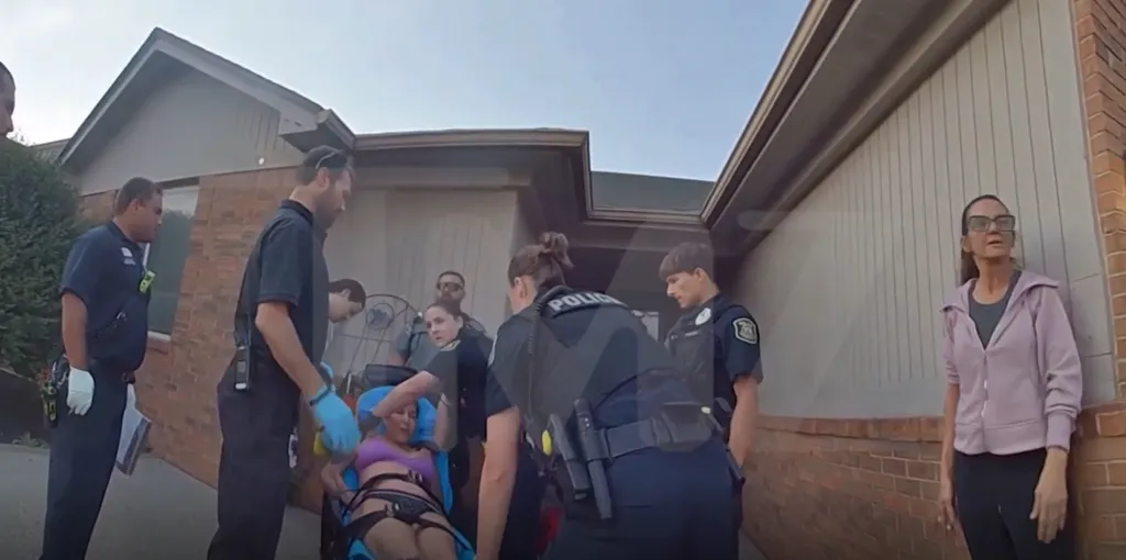 Paramedics and police respond to a medical emergency, with a woman being placed on a stretcher while others observe.