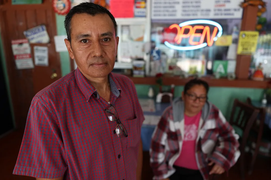 Miguel Carranza, owner of El Corredor restaurant, in a red and blue plaid shirt with his wife Irma Diaz in the background.