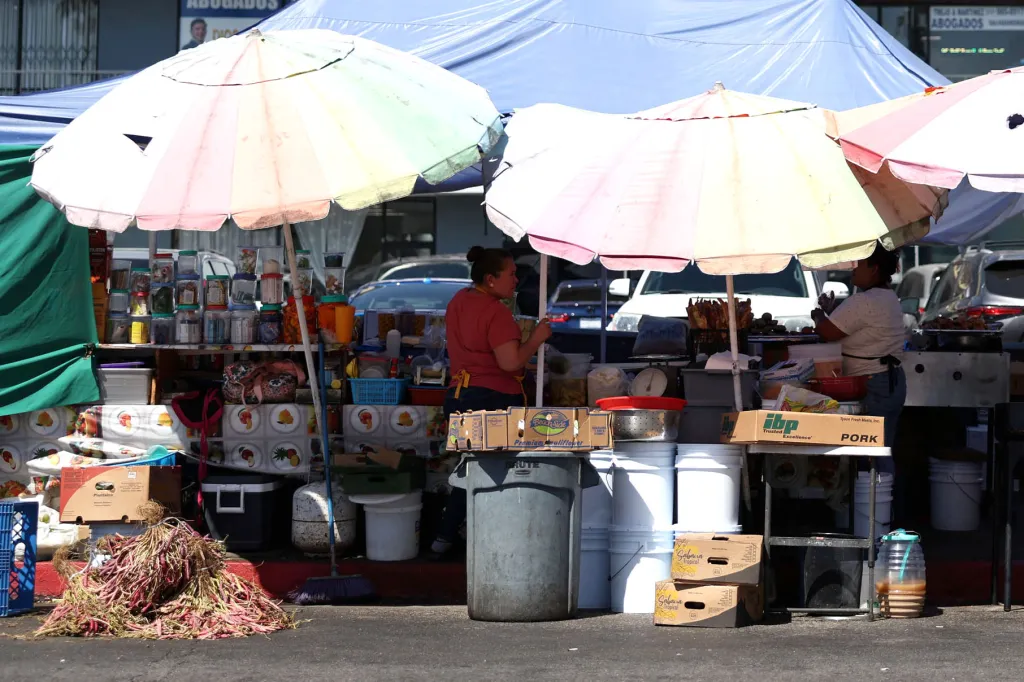Illegal street vendors set up under umbrellas, with goods displayed in front of them in the El Salvador Corridor in Los Angeles.