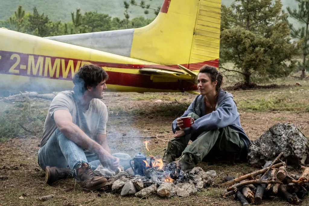 Jacob Elordi and Margaret Qualley sitting by a campfire in a scene from 