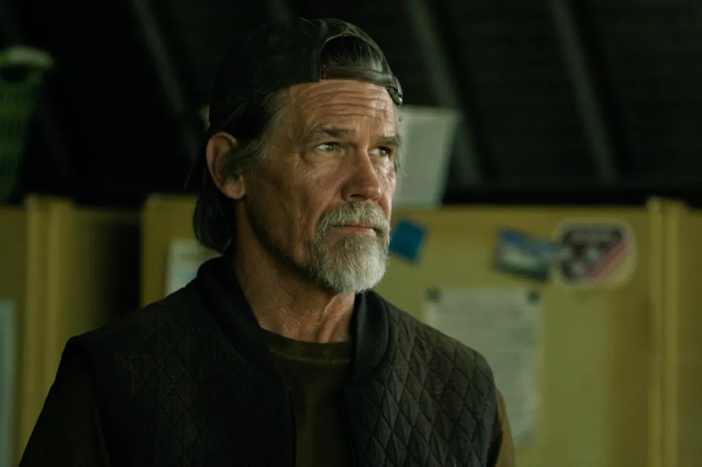 Josh Brolin with a beard and wearing a baseball cap and quilted vest in a scene from 