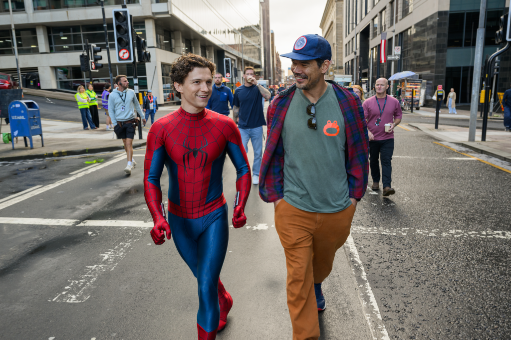 Tom Holland in a Spider-Man suit with director Destin Daniel Cretton on a city street.