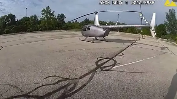 A silver helicopter landed in a parking lot.