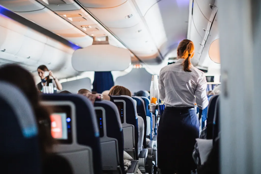 Flight attendant in uniform walking down the aisle of an airplane, serving passengers.