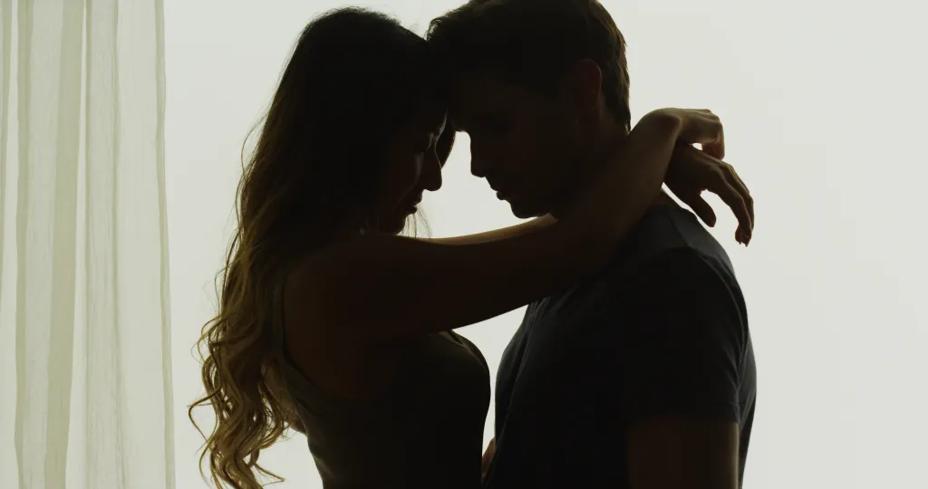 Silhouettes of an Asian woman and a Caucasian man with their heads touching and arms around each other.