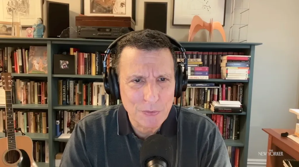 David Remnick, editor of The New Yorker, speaking into a microphone while wearing headphones in front of a bookshelf.