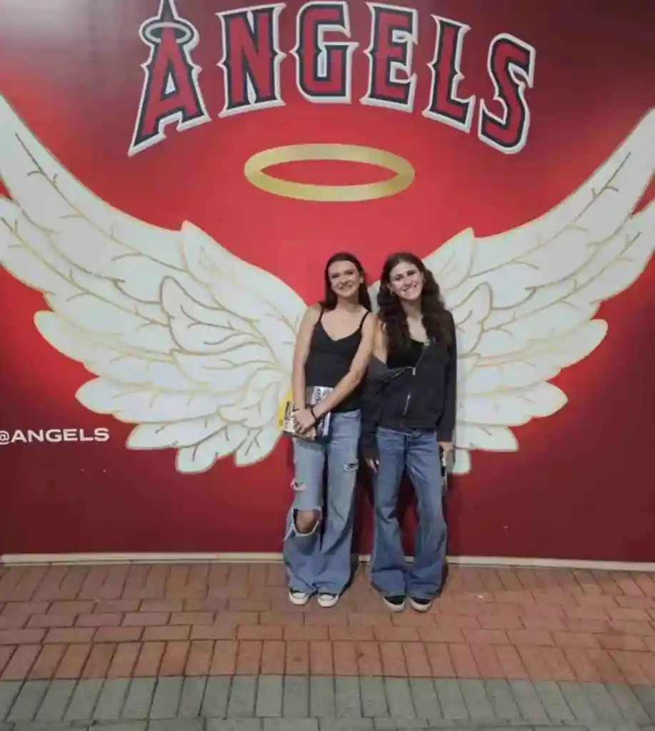 Isabell Hill and Maddalyn Dailey posing in front of a red wall with white angel wings and a halo.