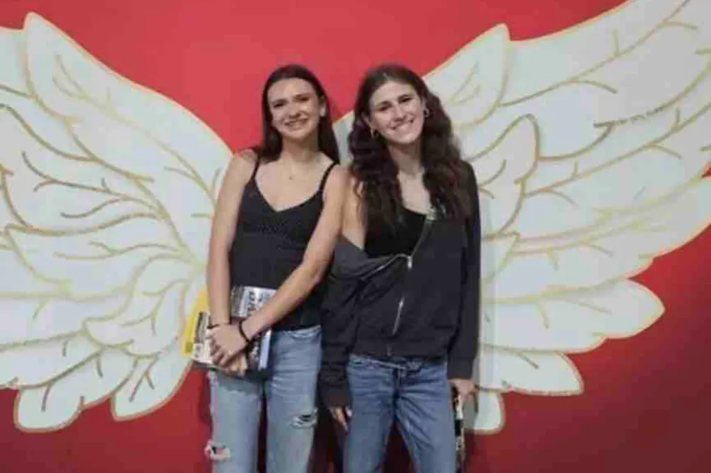 Isabell Hill and Maddalyn Dailey smiling in front of a red wall with white angel wings painted on it.
