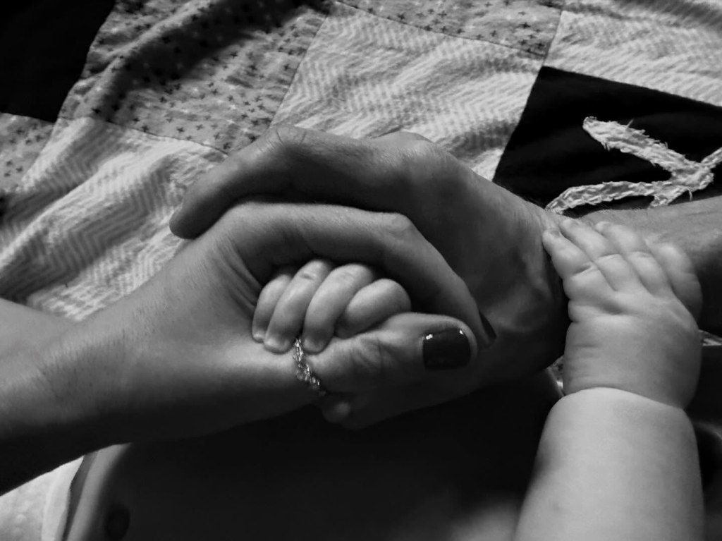 Black and white photo of three hands, one baby and two adults, interlocked.