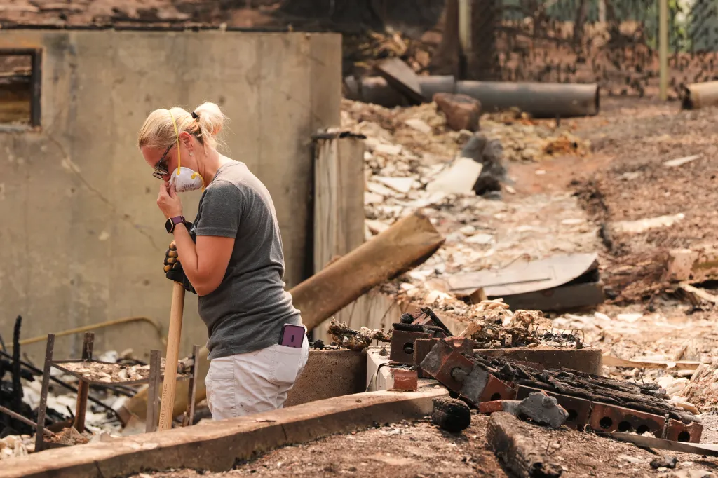 Jana Jensen sifts through the remains of her parents' home after a wildfire hit the northern part of Spokane, Wash., Monday, Aug. 3, 2026.