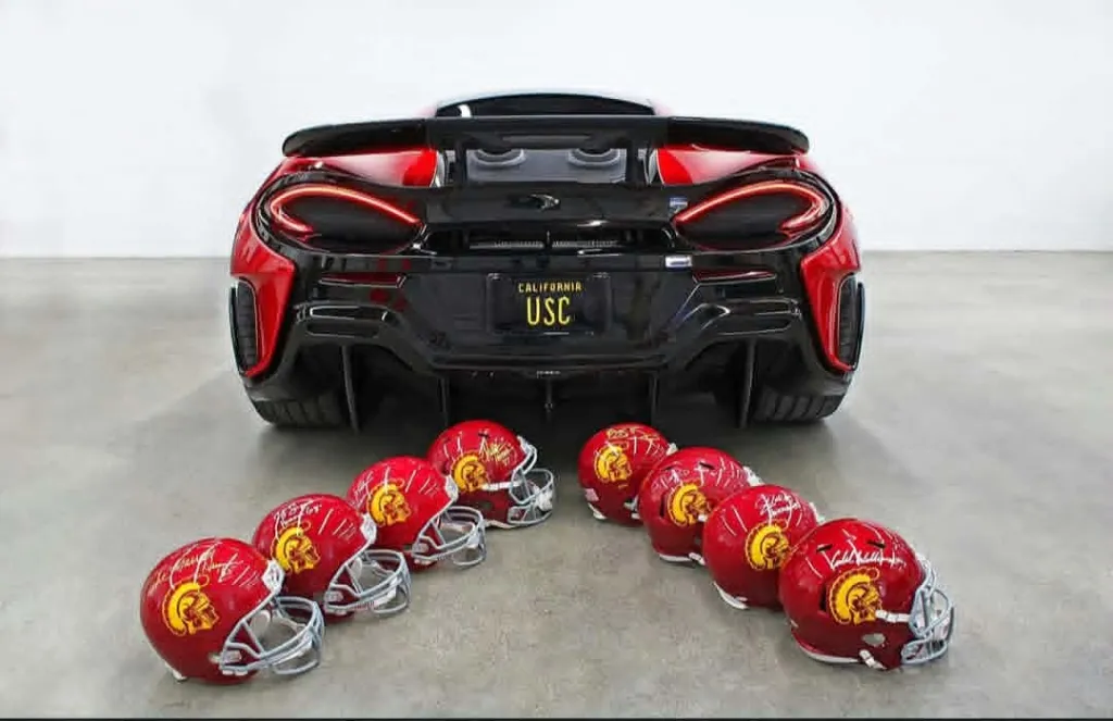 Red sports car with a USC license plate and several small USC helmets on the ground.