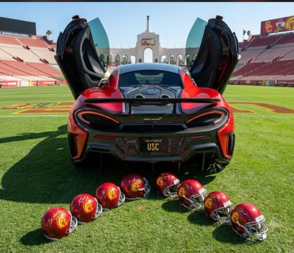 Red McLaren car with a USC license plate on a football field with helmets in the foreground.