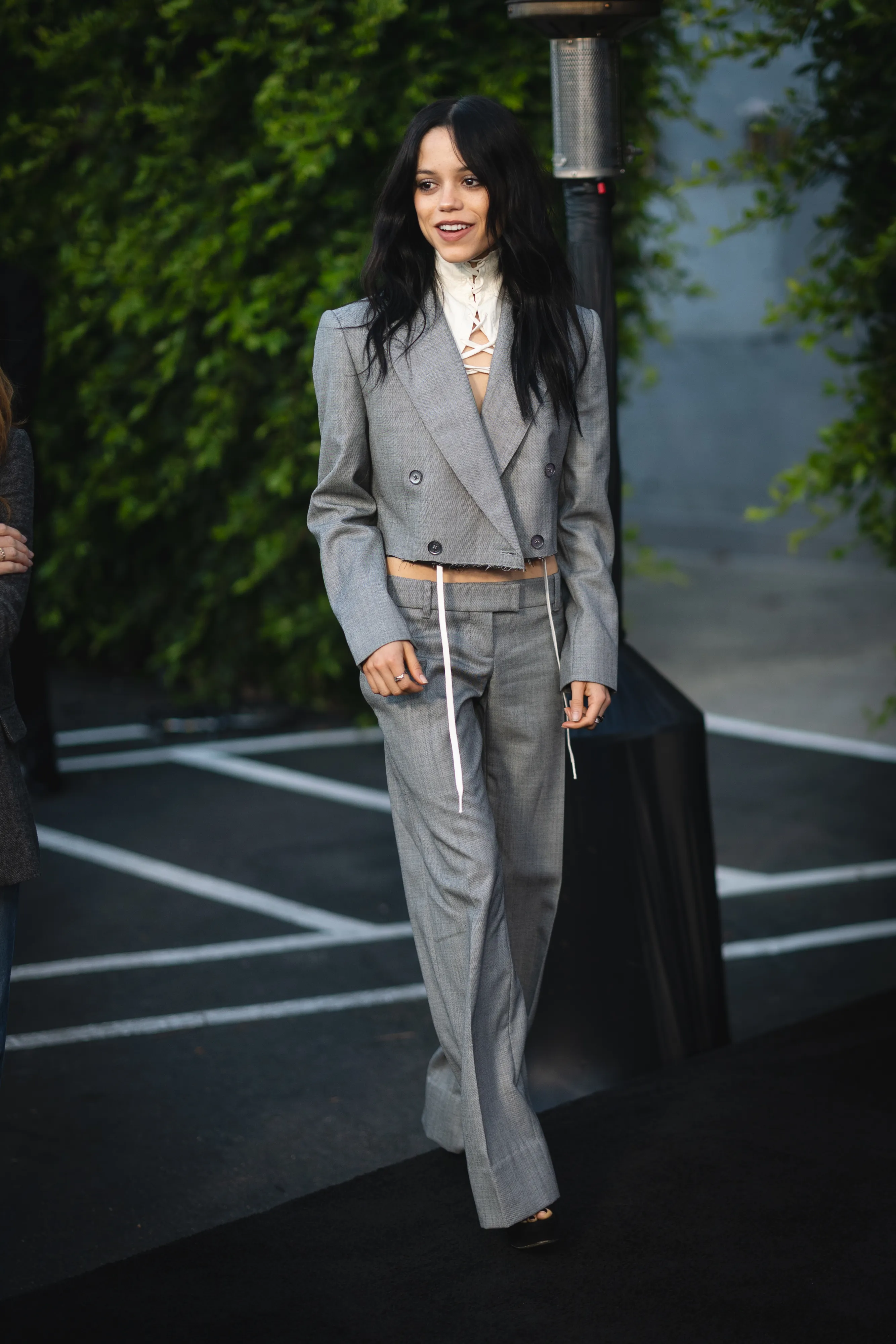 Jenna Ortega wearing a gray cropped suit with a white laced top.