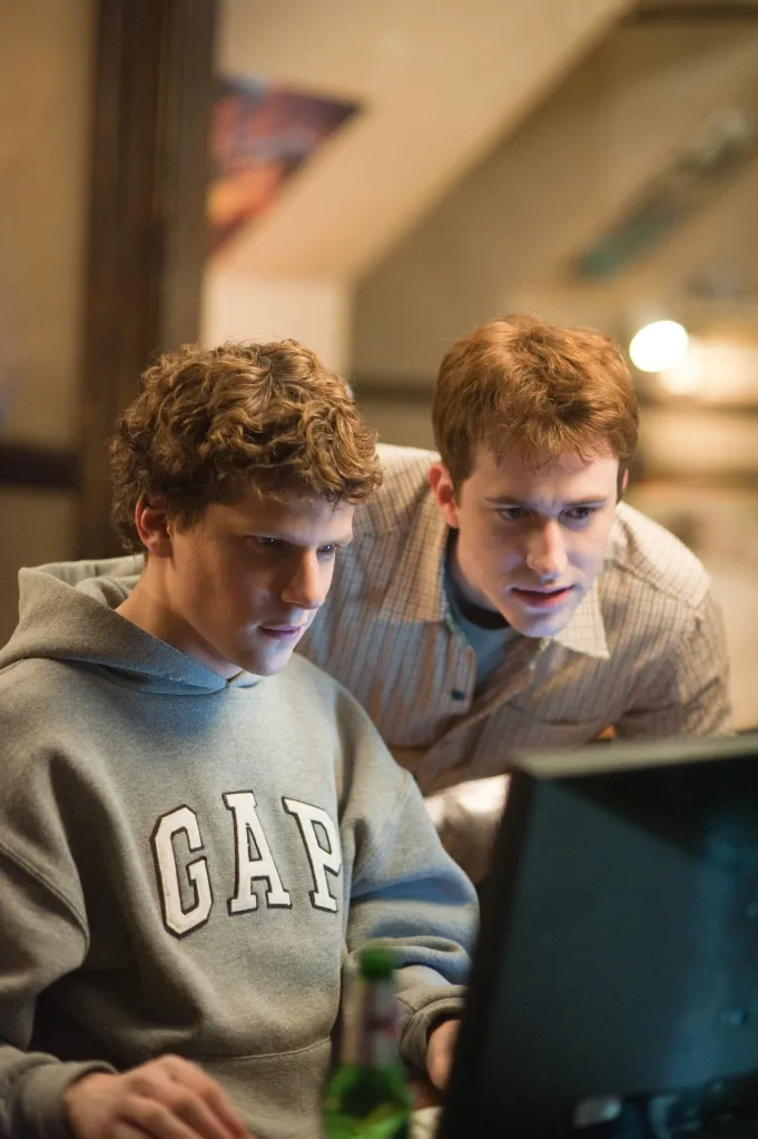 Jesse Eisenberg and Joseph Mazzello intently looking at a computer screen.