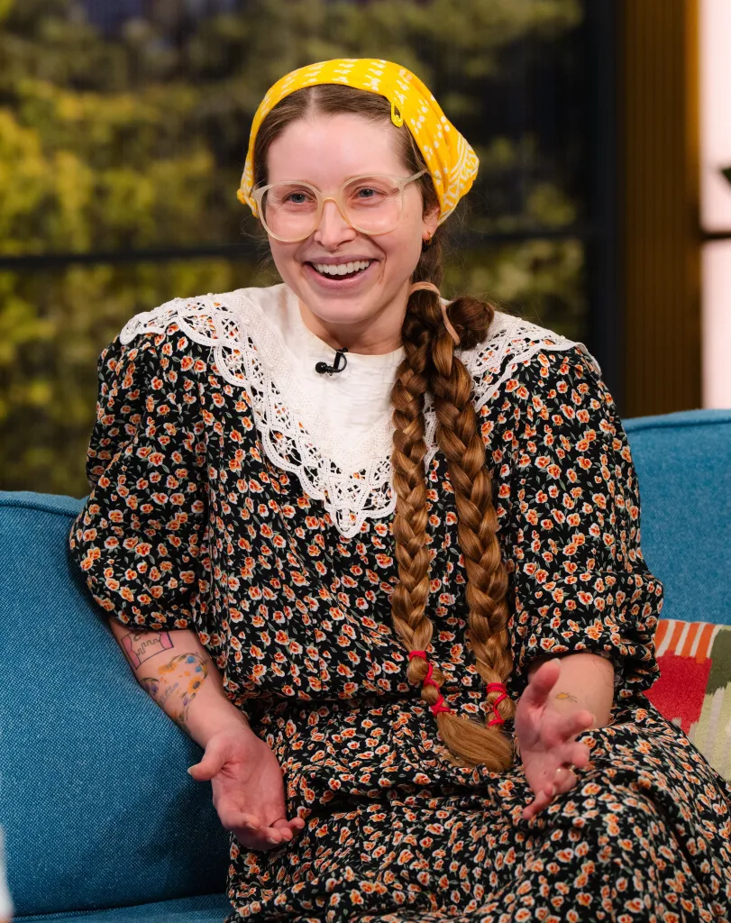 Jessie Cave smiling while sitting on a blue couch during the 