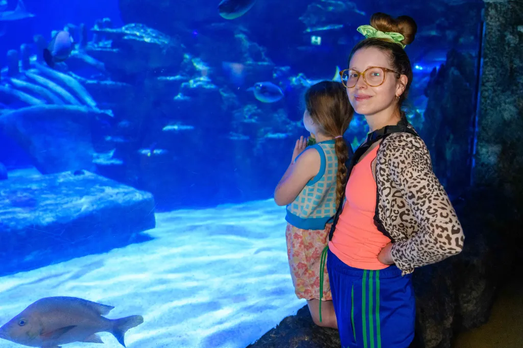 Jessie Cave and her daughter watching fish in a large aquarium tank.