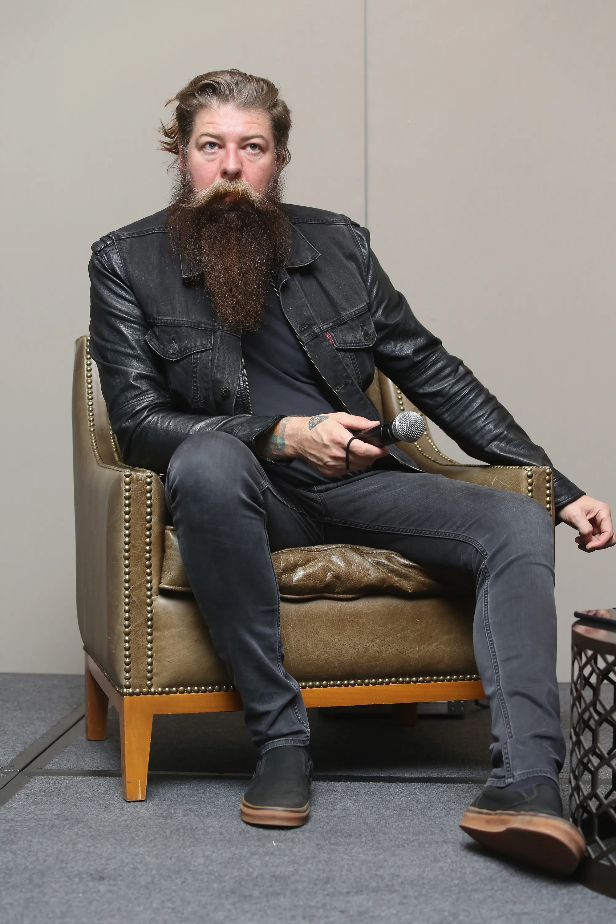 Jim Root of Slipknot sitting in a brown leather armchair, holding a microphone.