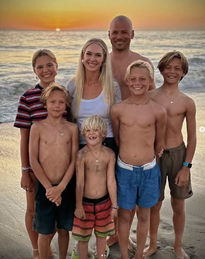 Josh Collette and his family of five children standing on a beach at sunset.