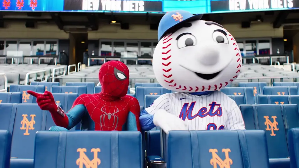 Spider-Man and Mr. Met mascot sitting in a baseball stadium.
