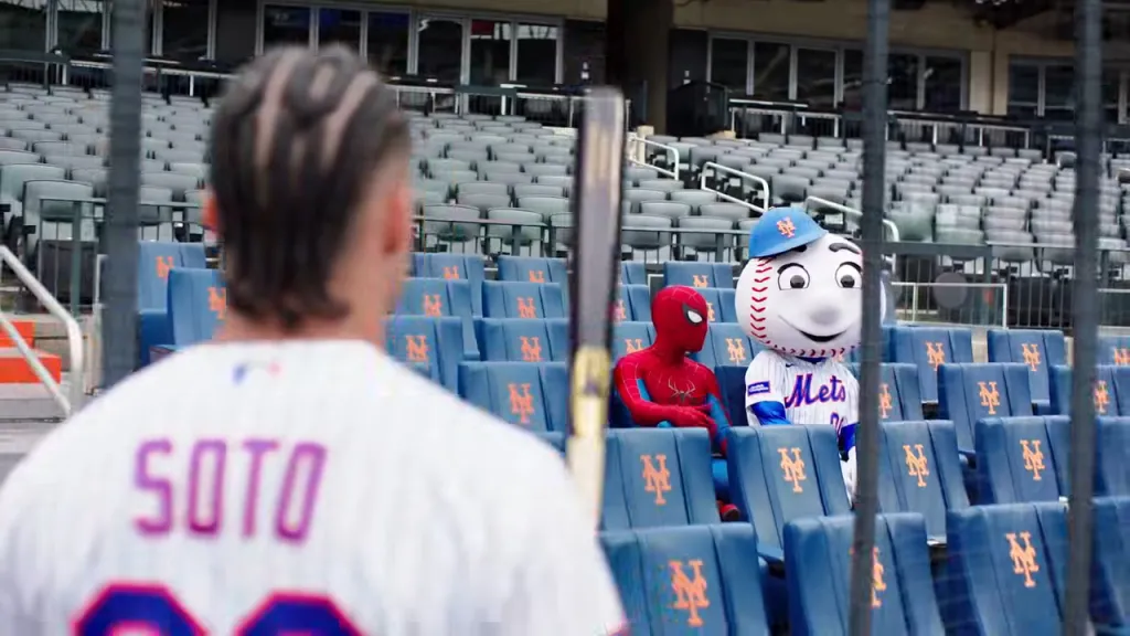 Juan Soto looking over his shoulder at Spider-Man and Mr. Met sitting in the stands.