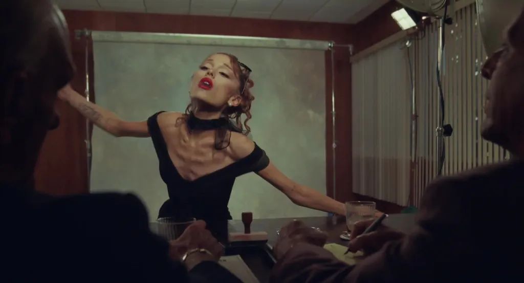 Ariana Grande in a black dress at a table with two men in suits.