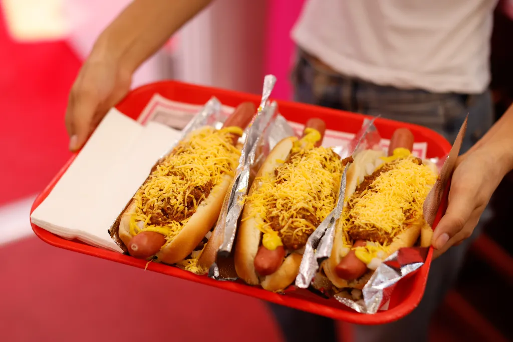 Chili dogs with shredded cheese on a red tray.