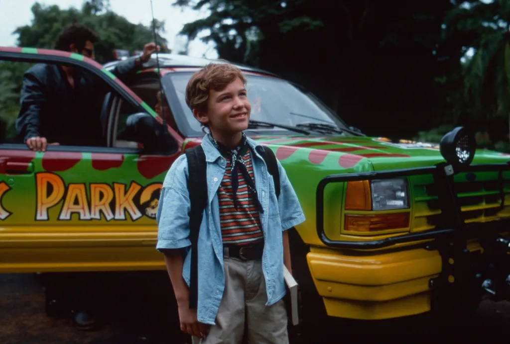 Joseph Mazzello as Tim Murphy, standing in front of a Jurassic Park jeep.