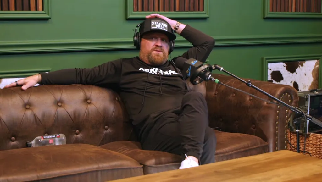 Justin Moore sitting on a leather couch with headphones and a microphone.