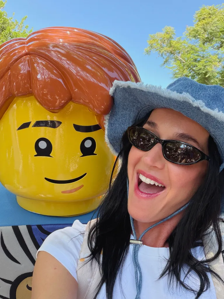 Katy Perry poses next to a giant Lego head.