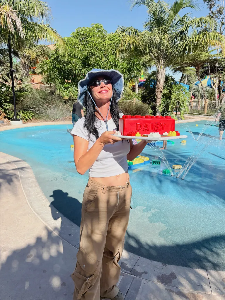 Katy Perry holding a red Lego-themed cake that reads 