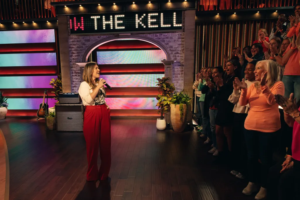 Kelly Clarkson on her talk show set, addressing an audience who are clapping.
