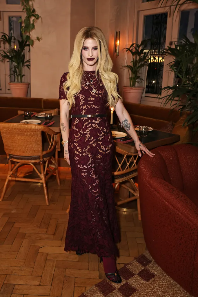 Kelly Osbourne in a deep red lace gown with long blonde hair, standing in a restaurant.