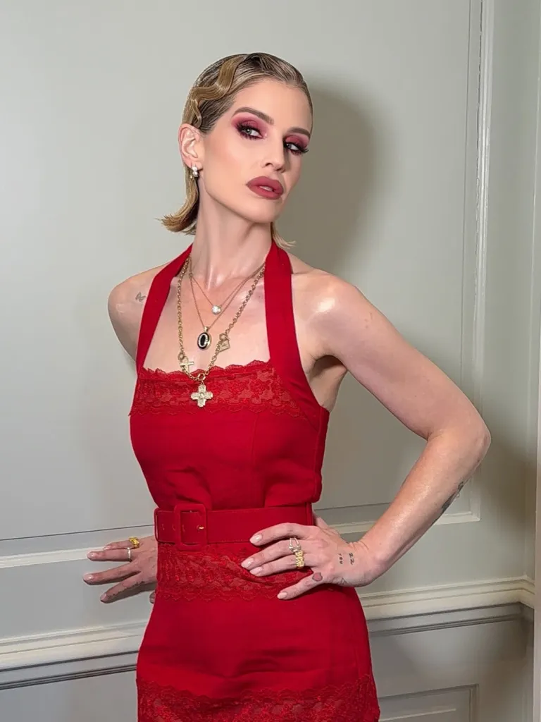 Kelly Osbourne in a red lace-trimmed dress, with dark pink eye makeup and wavy blonde hair.