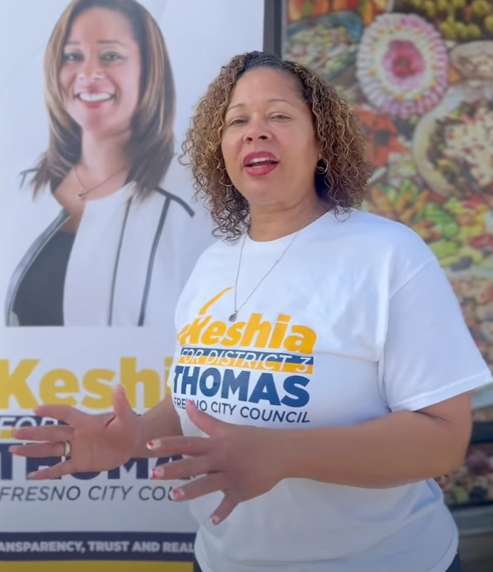 Keshia Thomas speaking in front of a campaign poster for Fresno City Council.